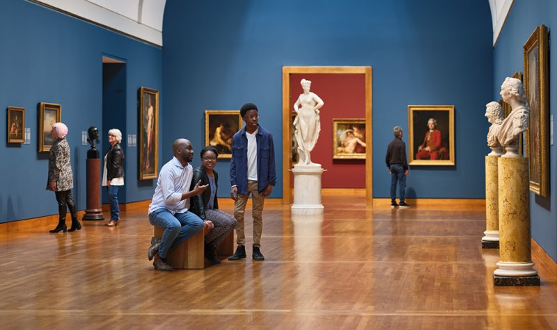 Visitors discussing and looking at paintings and sculptures in the European and American Galleries.