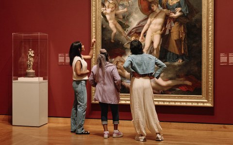 Three persons looking at a large artwork in a red room.