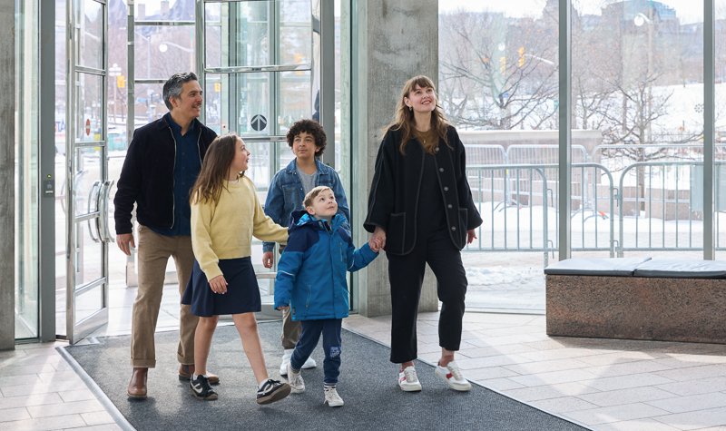 Two adults and three children enter the Gallery through the glass doors of the Main Entrance.